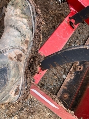 black boots covered in mud being scrapped off on a red tractor implement