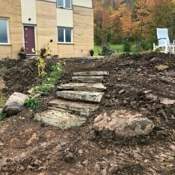 large flagstone steps to a concrete patio. patio chairs, a house and coloured leaves on trees in the background