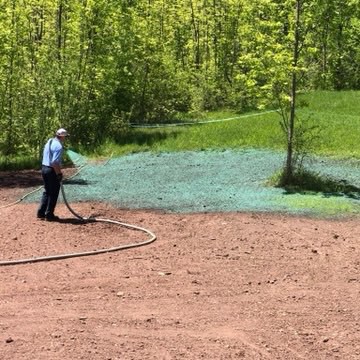 a man with a hose over his shoulder, spraying green material onto the dirt