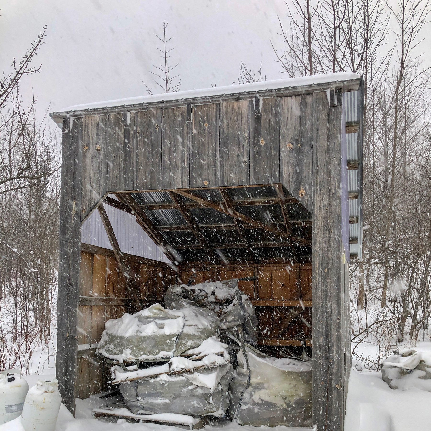 large bags of firewood inside a shelter with snow falling