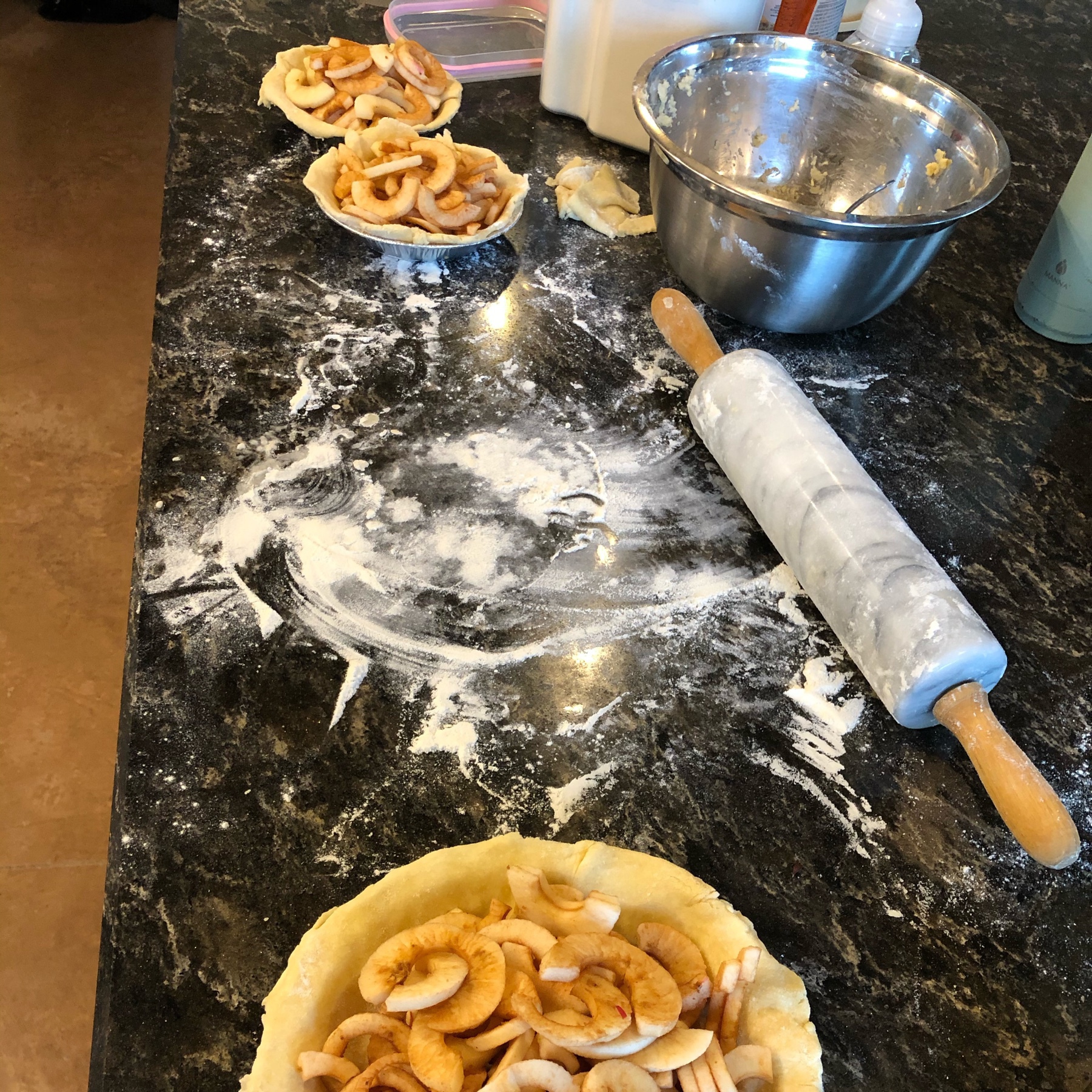apple pieces in 3 pie shells with flour and a rolling pin on a countertop