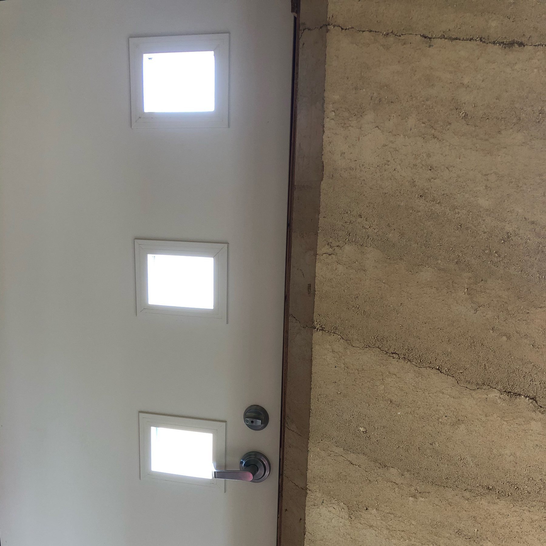 three small windows in a door next to a rammed earth wall