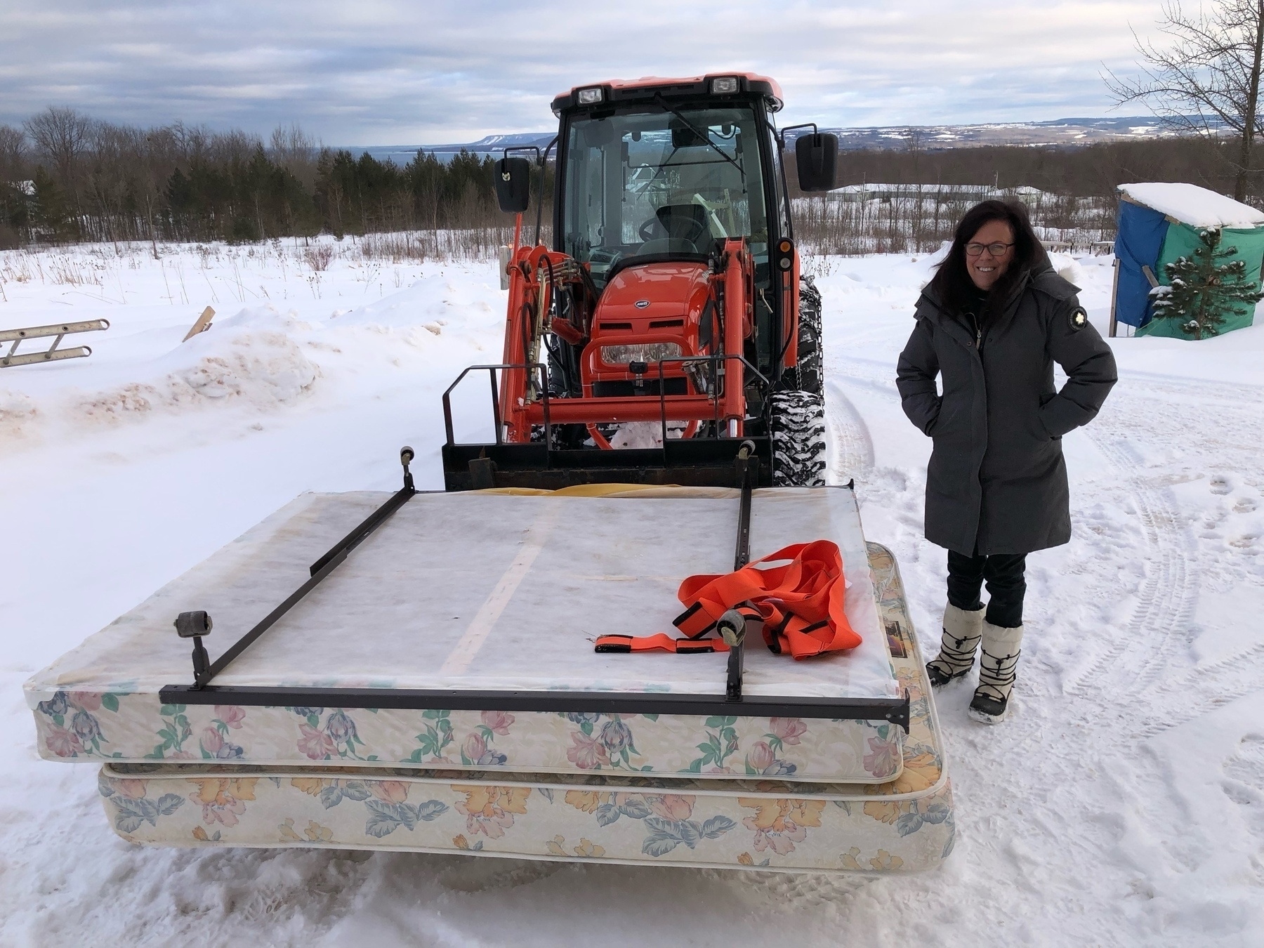bed in front of a tractor; a lady is standing beside, surrounded by snow