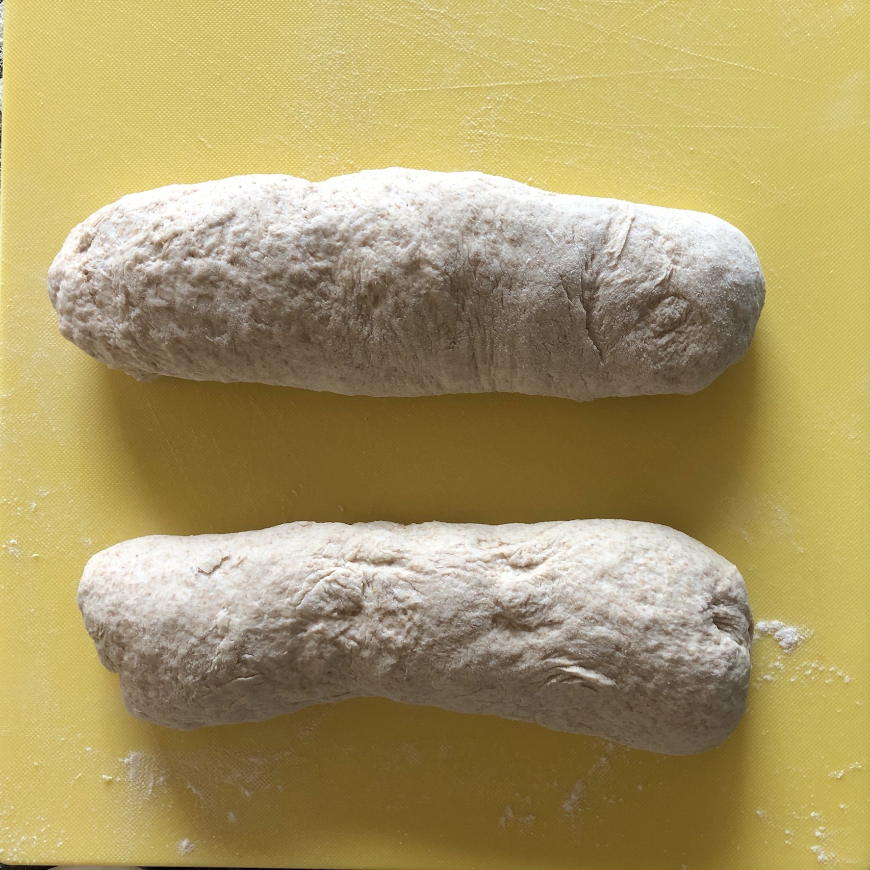 Two log rolls of dough on a yellow board