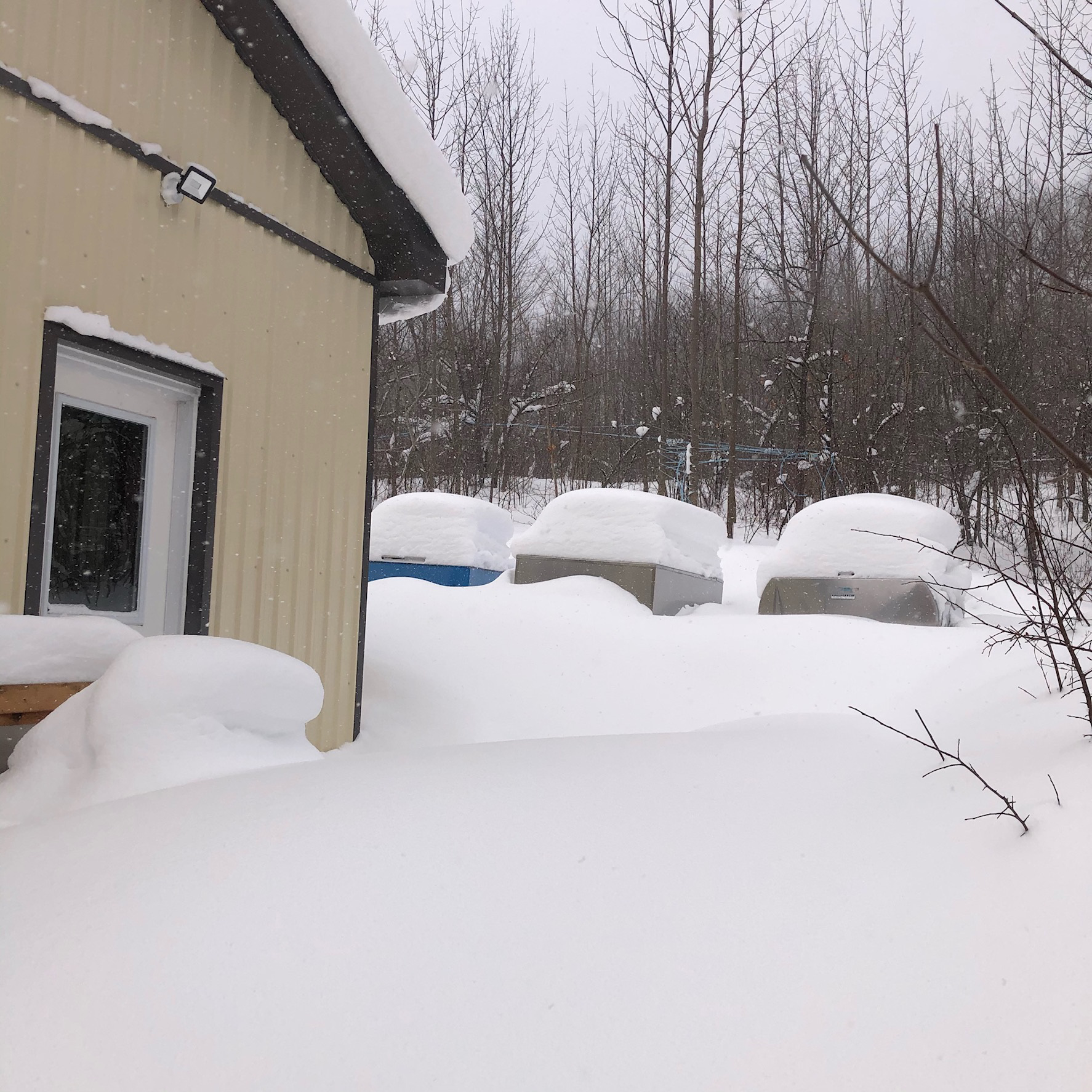 three metal tanks, covered in 60+cm of snow. there is a yellow building beside them.