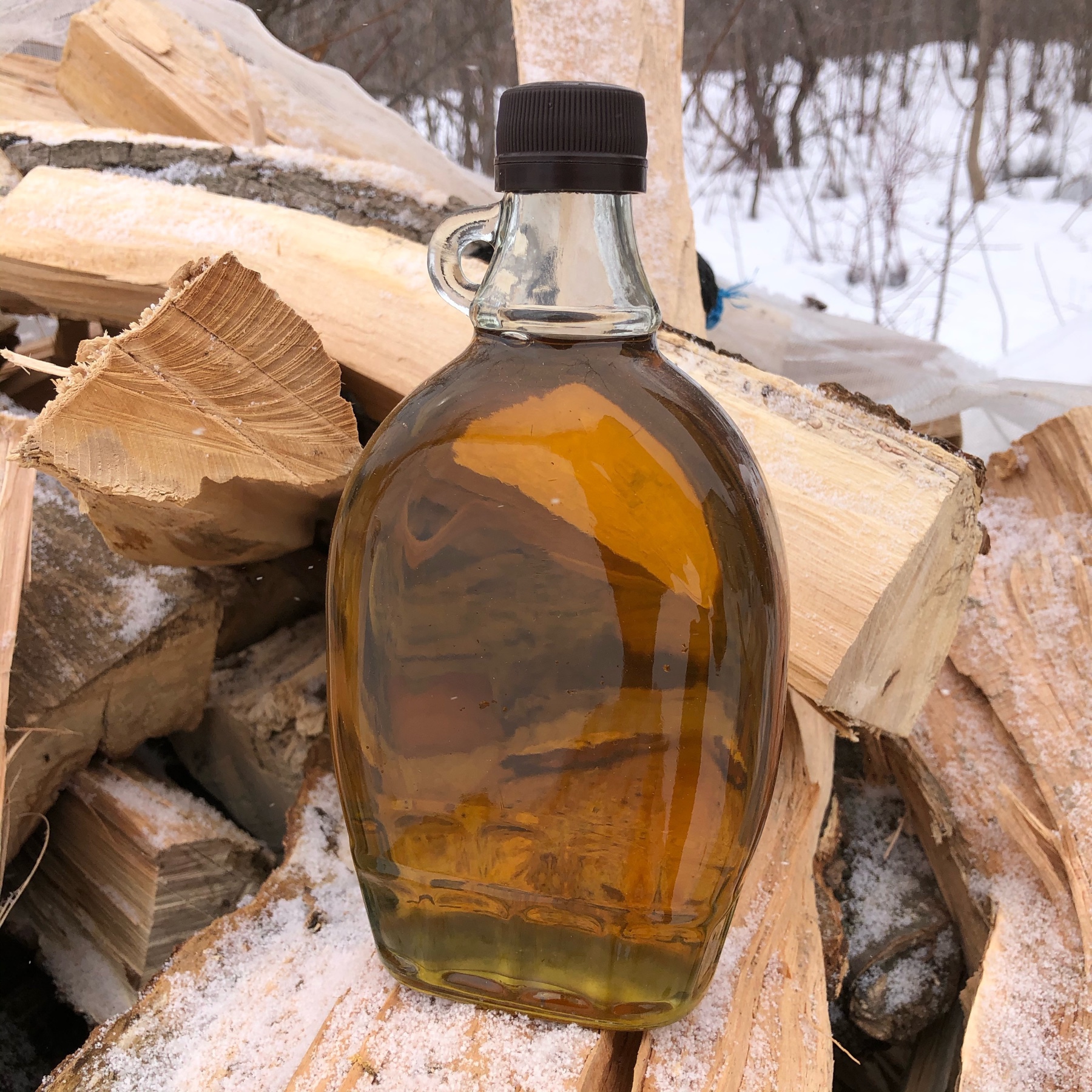 500 ml bottle of light maple syrup sitting on splits of maple firewood 