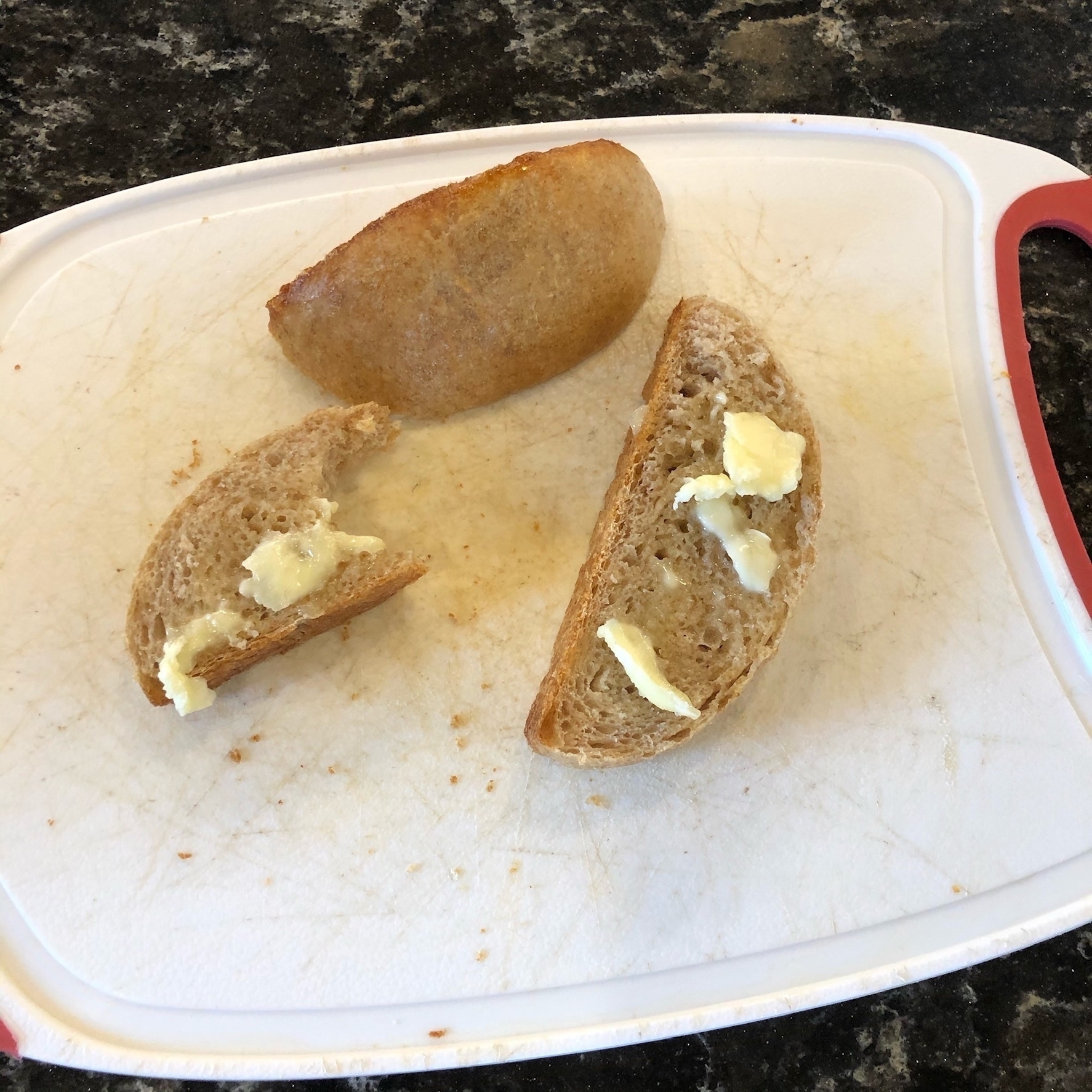 Three small slices of bread with pads of butter on top, sitting on a white cutting board