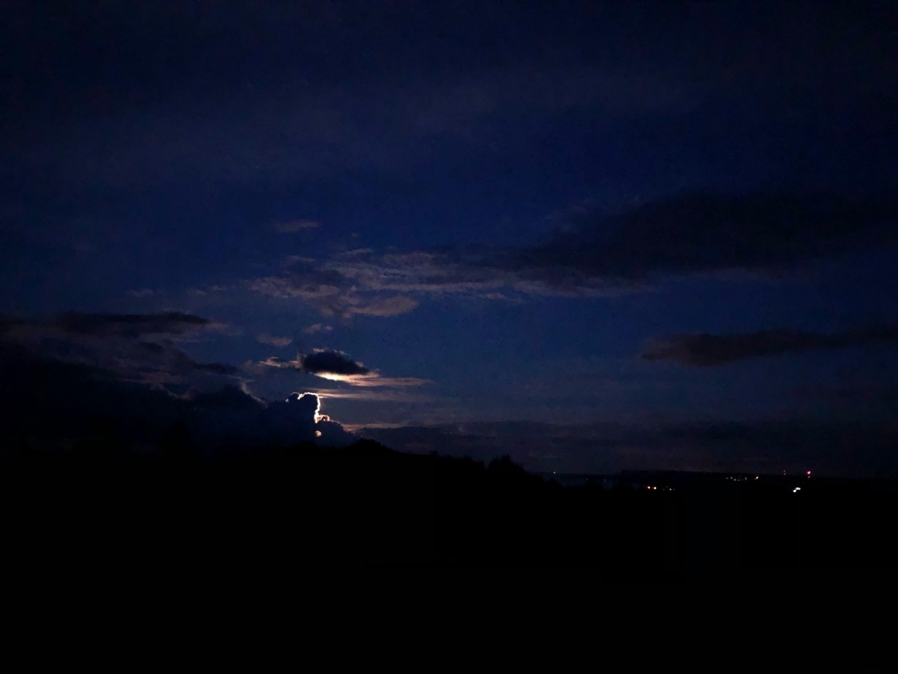 rising moon backlighting dark clouds with a few lights visible in town