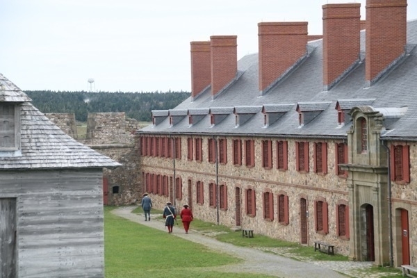 soldiers walking in front of a large stone building. there is a wooden building on the left