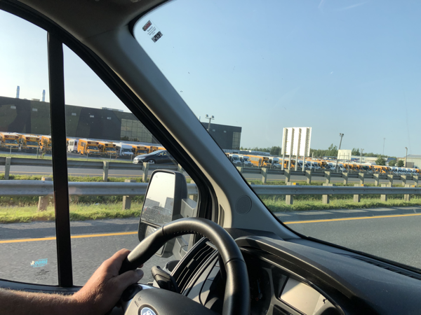 drivers hands on the steering as the vehicle passes a parking lot full of school buses