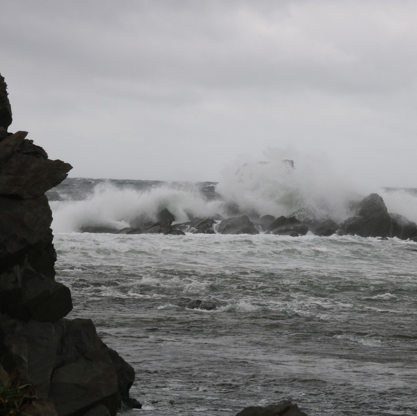 waves crashing over rocks. there is a rock wall on the left side